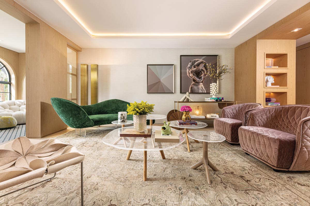 An illuminated ceiling treatment and built-in display shelves give the living room a soft ambient glow. Shapely lounging pieces pair with a cluster of round Plexiwood coffee tables, lending an organic vibe to the space. A composition of artworks by Marcio Ponte (left) and Mono Giraud (right) creates a visually compelling focal point.