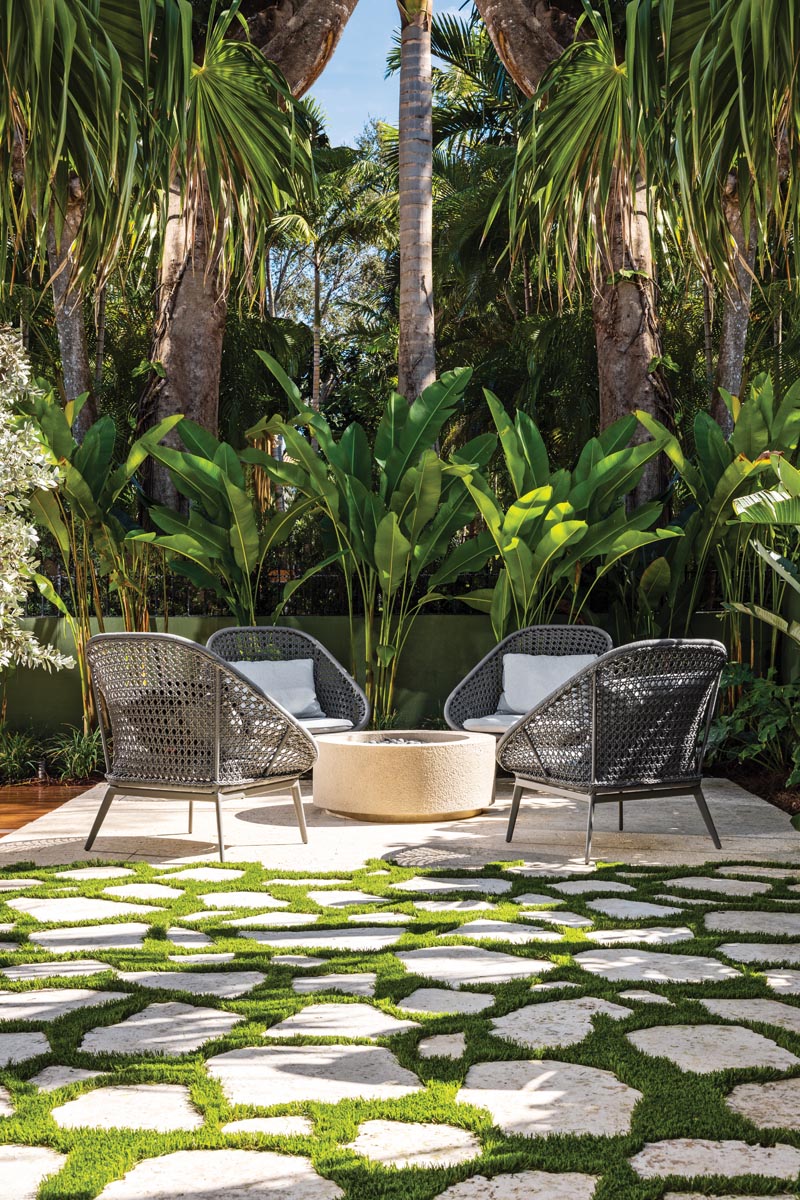 An intimate seating area amidst the native foliage centers around a fire pit where friends gather for evening cocktails. A series of stepping stones pave the lush lawn, adding an elegant walkway to this charming setting. The dense greenery and towering palms add privacy and natural beauty.