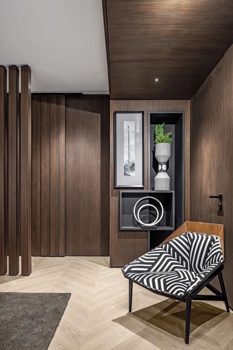 A custom art niche integrated into a wood paneling system creates a focal point in the primary suite entrance hall. Accented with a dazzling black-and-white patterned vintage chair, the clever millwork system includes hidden storage.