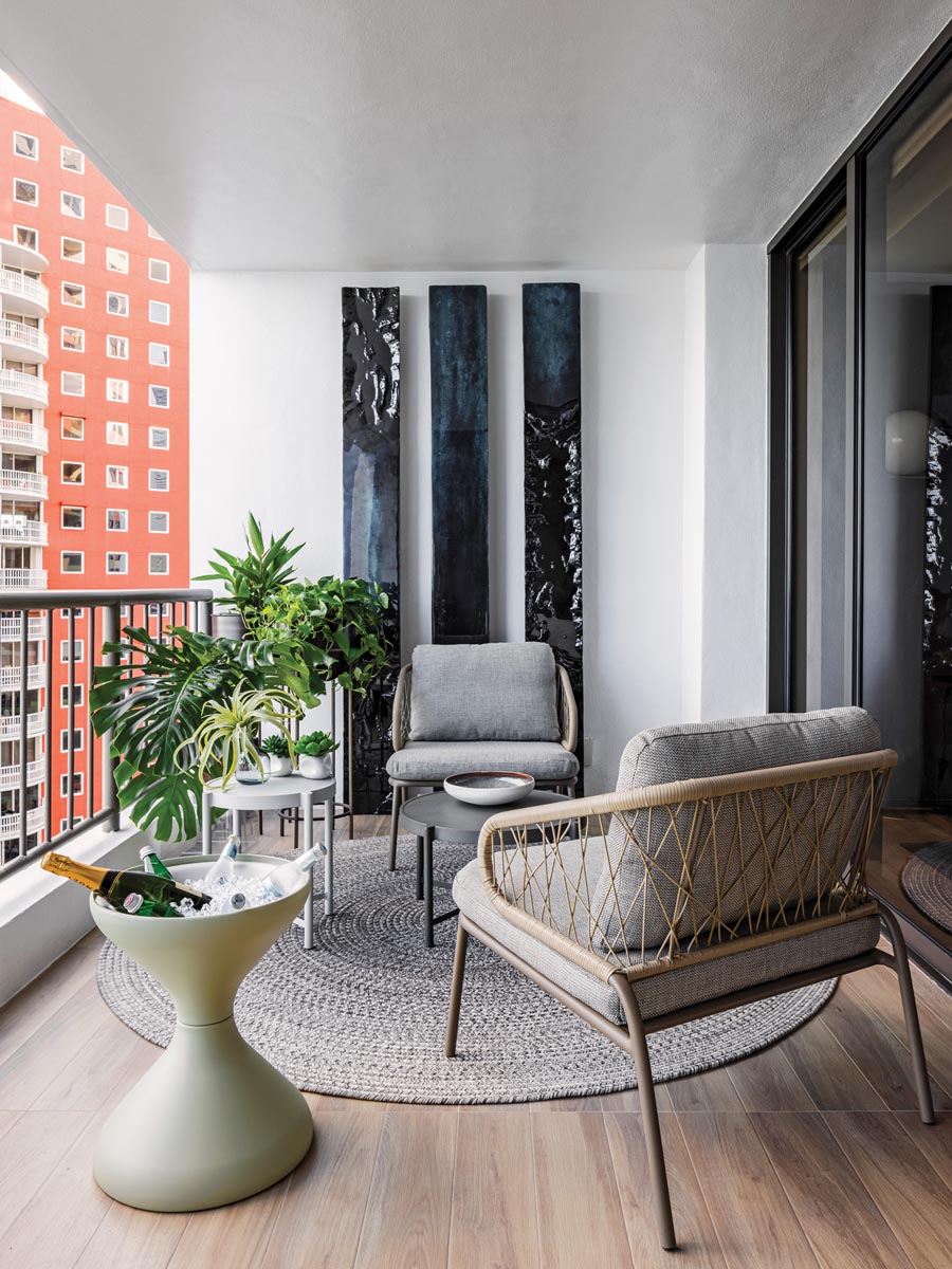 The fully furnished outdoor terrace features a striking wall treatment composed of a trio of painted panels by Brazilian artist Andre Poli. A textural woven rug by Gloster anchors sculptural seating pieces from Harmony Studio. The fluid lines of a contemporary wine cooler emit an organic vibe.