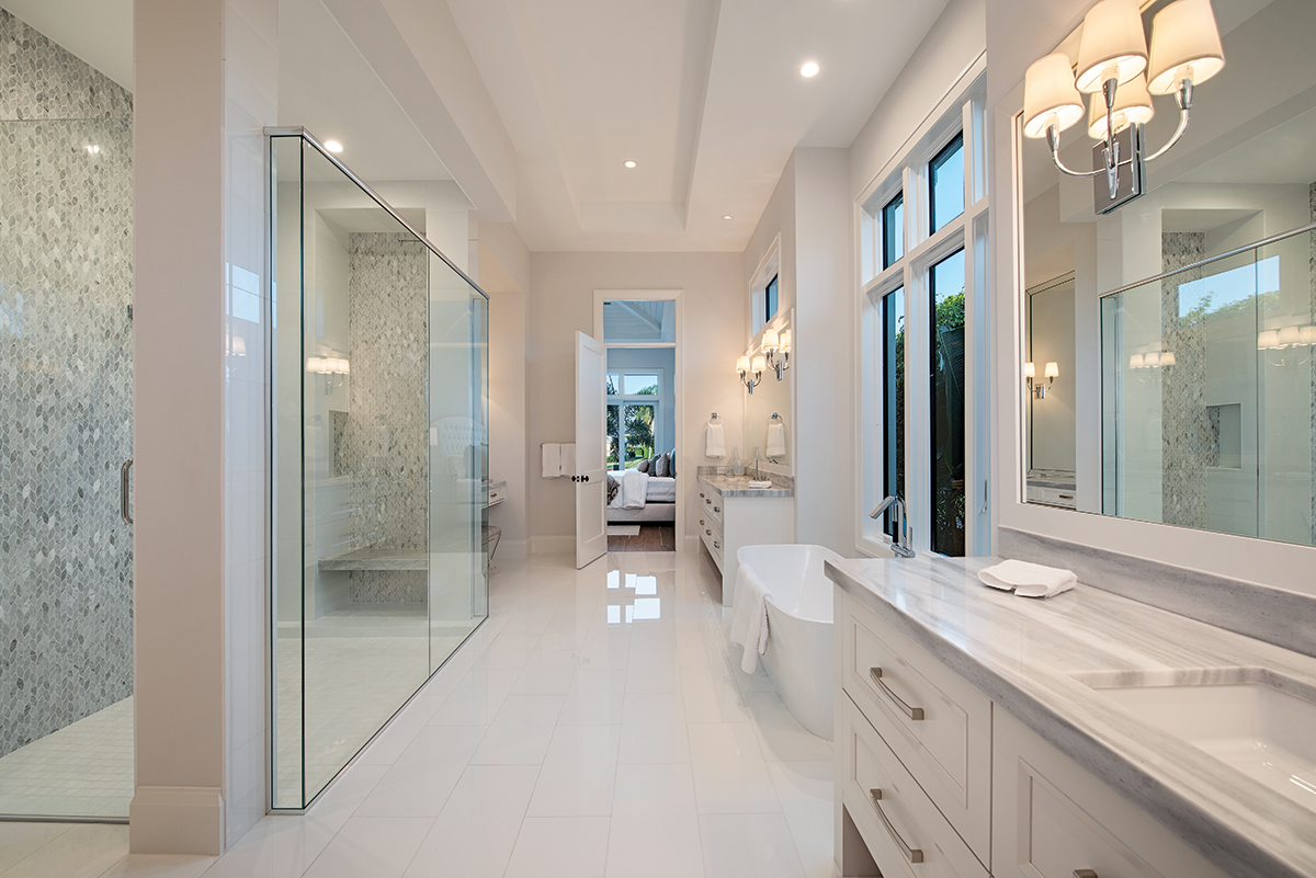 Clean lines, polished tile flooring, an expansive shower, and white vanities topped in Rain Forest Marble’s pearl gray striation opens up the master bath. A picture window with lush garden views provides the perfect backdrop for the Victoria & Albert tub from Ferguson.