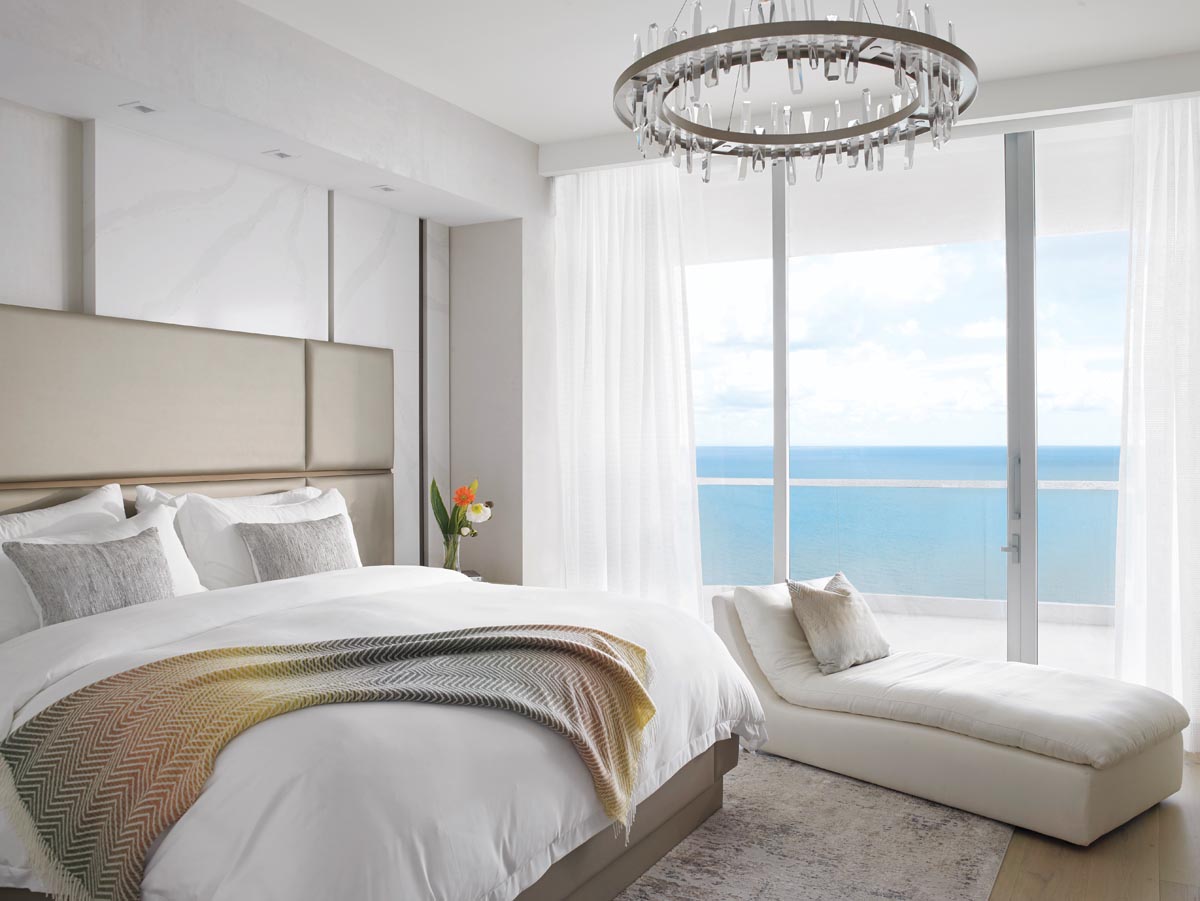 Ocean views are a given in the primary bedroom, which is anchored by a bespoke bed from DH Home. The chandelier by Solitude is one of two in the residence.