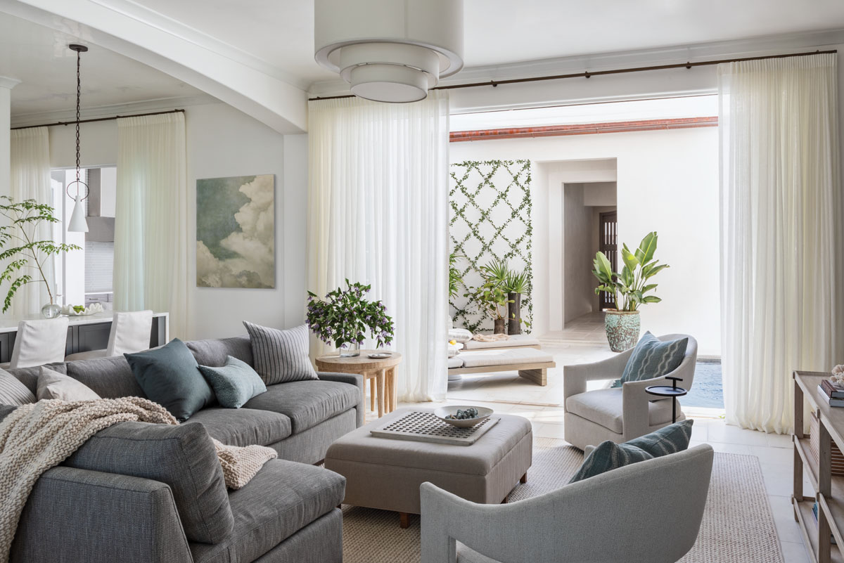 A large gray sectional with seafoam green pillows and two swivel chairs from McAlpine’s furniture line make the living room a comfort- able space where family can gather. Sheer curtains add softness to the area, making it a peaceful spot to unwind after a day at the beach.
