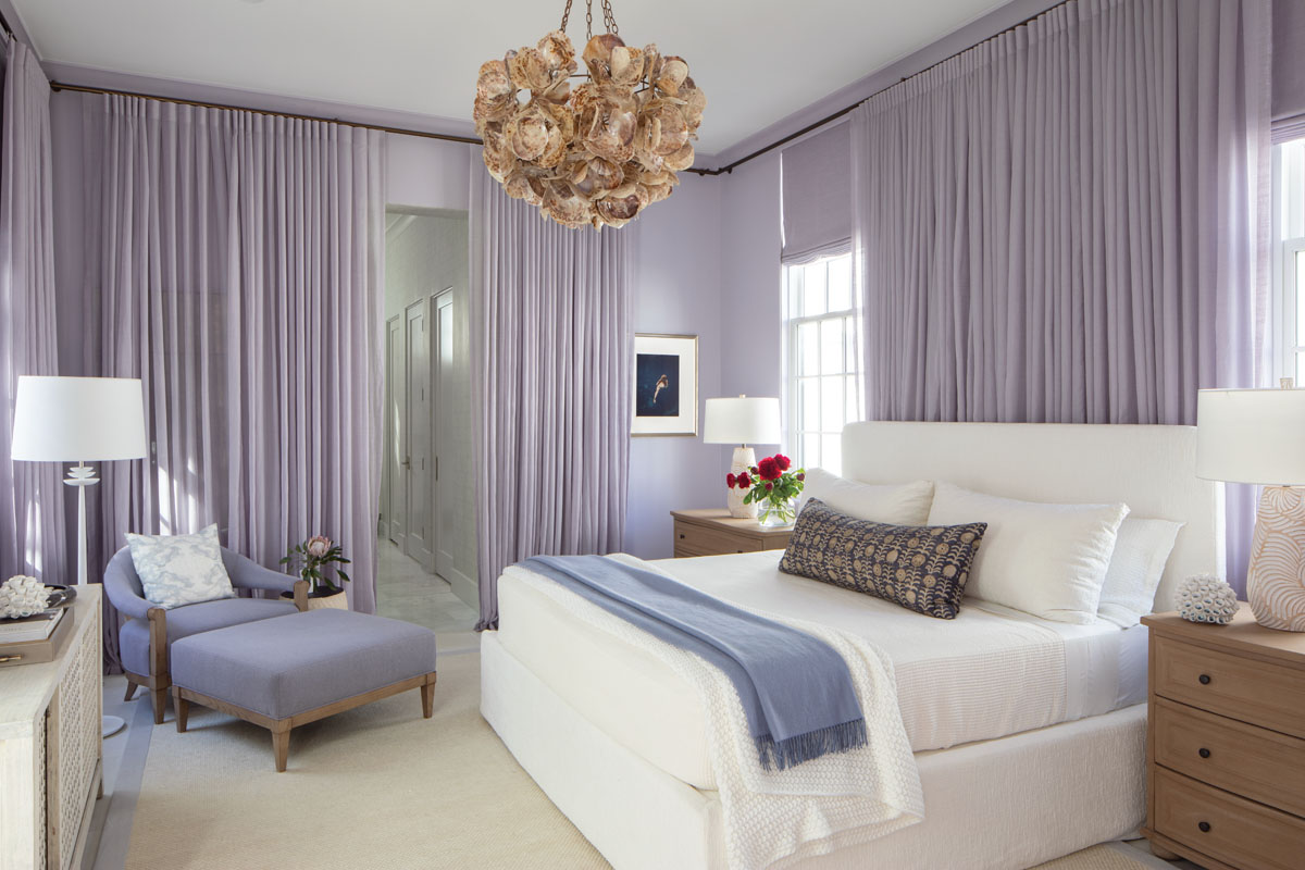 Booth opted for extensive lavender draperies in the master bedroom to envelop the space with a calming, soft hue. Elegant white linens and pale furnishings add to the serene ambiance, while a shell chandelier reminds us of the home’s beach location.