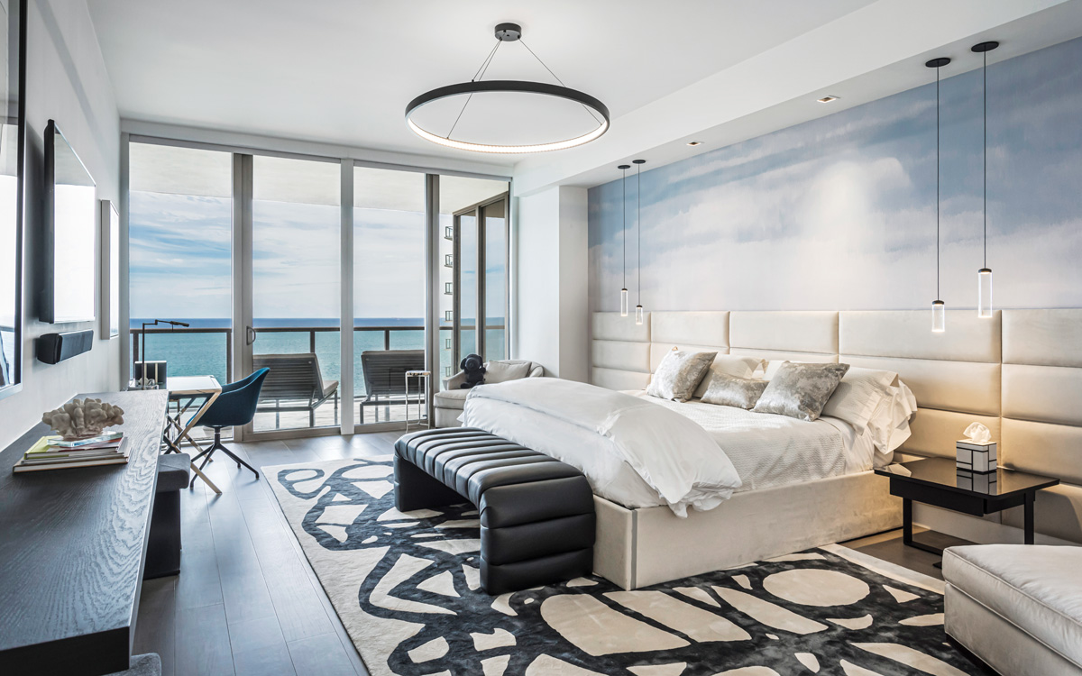 The ocean and sky outside are echoed in the blues of the custom mural behind the bed. Unlike the main traffic areas, this primary bedroom has wide-plank wood floors in a matte finish. The desk by the window is where the Morellis conduct many of their virtual meetings with their Manhattan law firm.