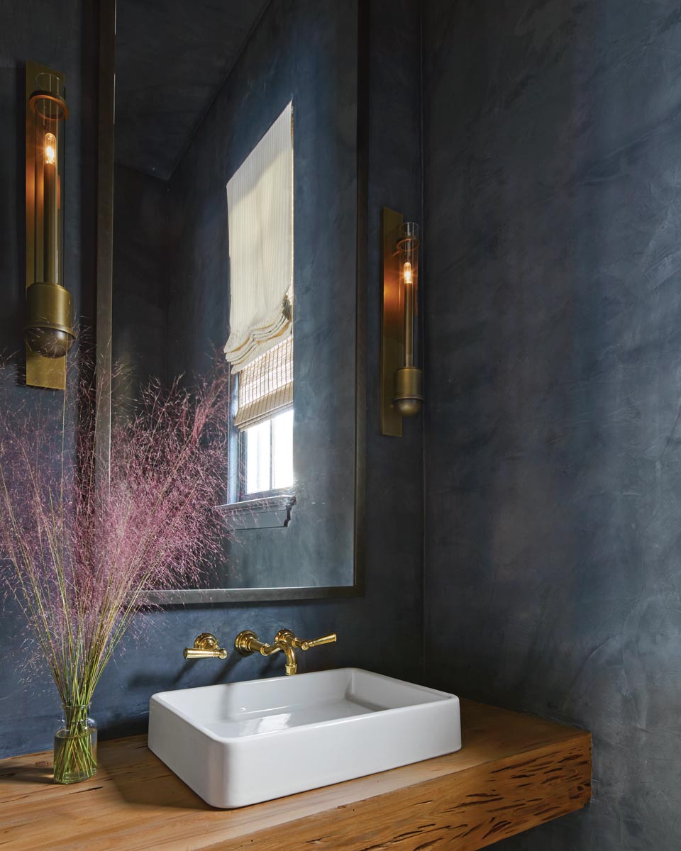A departure from the home’s otherwise bright aesthetic, the powder room is wrapped in rich black Venetian plaster walls illuminated with Urban Electric sconces. An unexpected pecky cypress vanity holds an elegant Waterworks vessel sink.