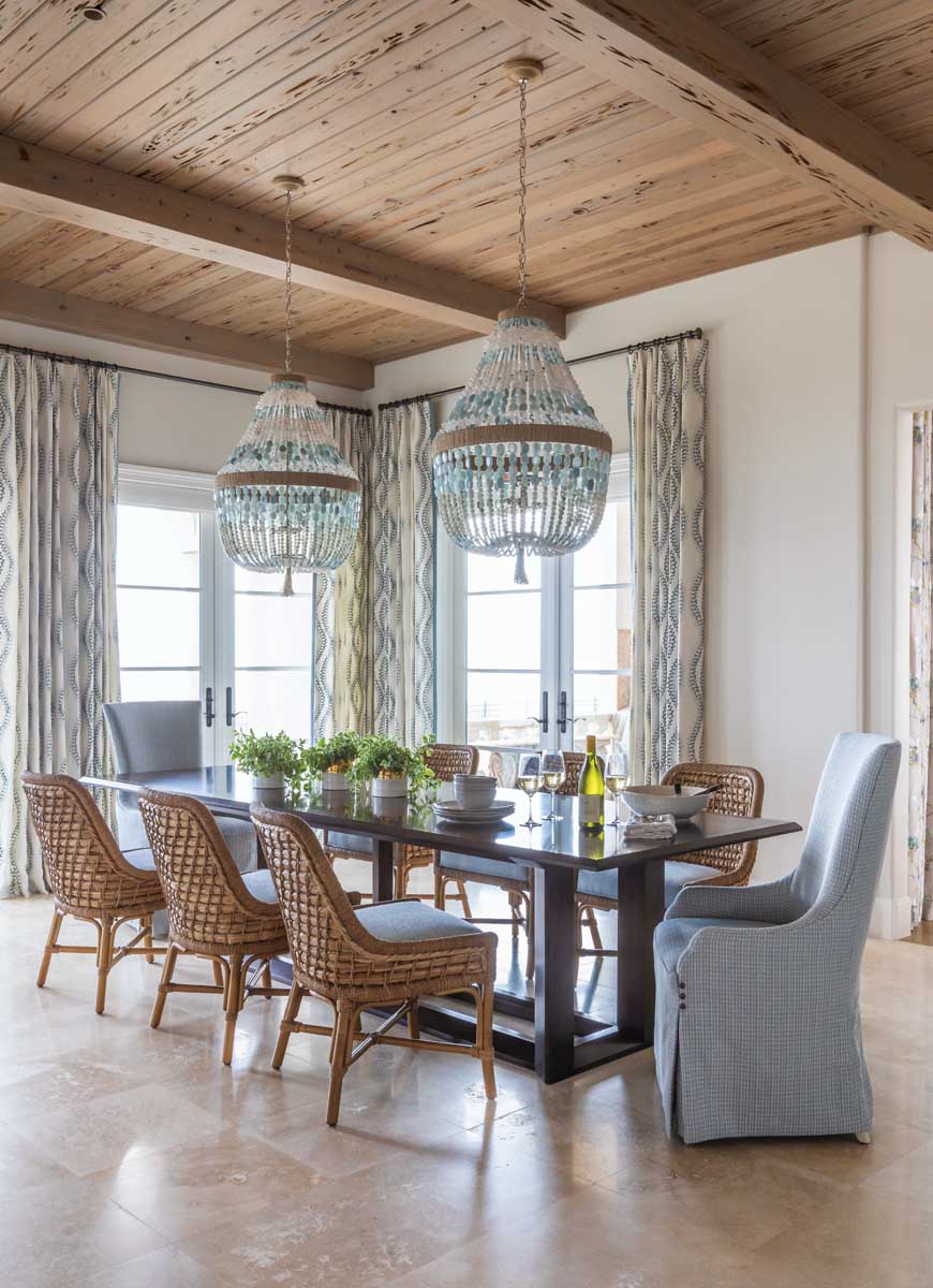 Rug-less travertine flooring in the breakfast room solidifies the home’s intended coastal feel. The cypress ceiling was white-washed to match the flooring tonally. The Ro Sham Beaux beaded chandeliers were chosen because they are large enough to be commanding without blocking the views.
