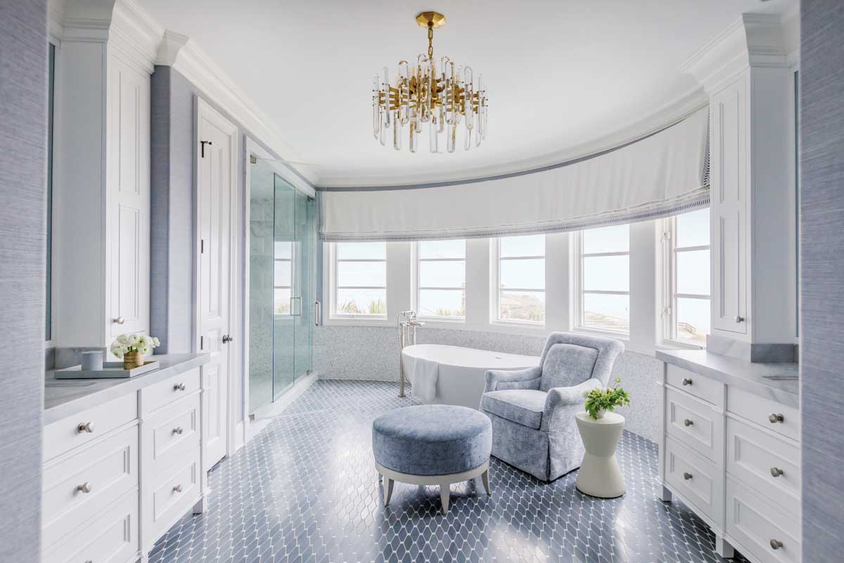 A sanctum of soft shades, the primary bathroom is clad in marble mosaic that glimmers when struck by natural rays from the curved windows or light from the optic crystal chandelier by Visual Comfort. A faux Roman valance hides electric shades that slide down to cover the windows from the strong light reflecting off the ocean.