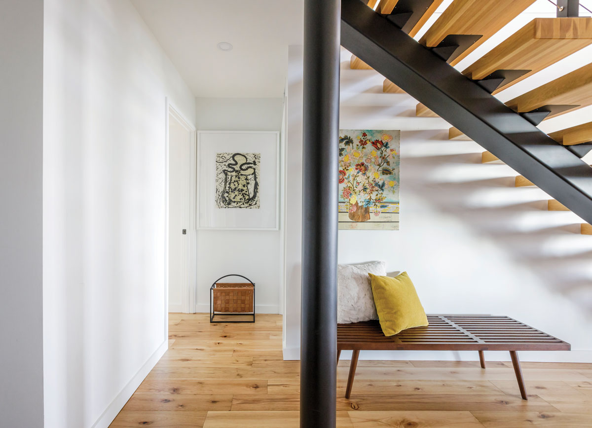 A cozy spot under the stairwell houses a wood-slat bench from the homeowners’ previous furniture collection, and abstract artwork.