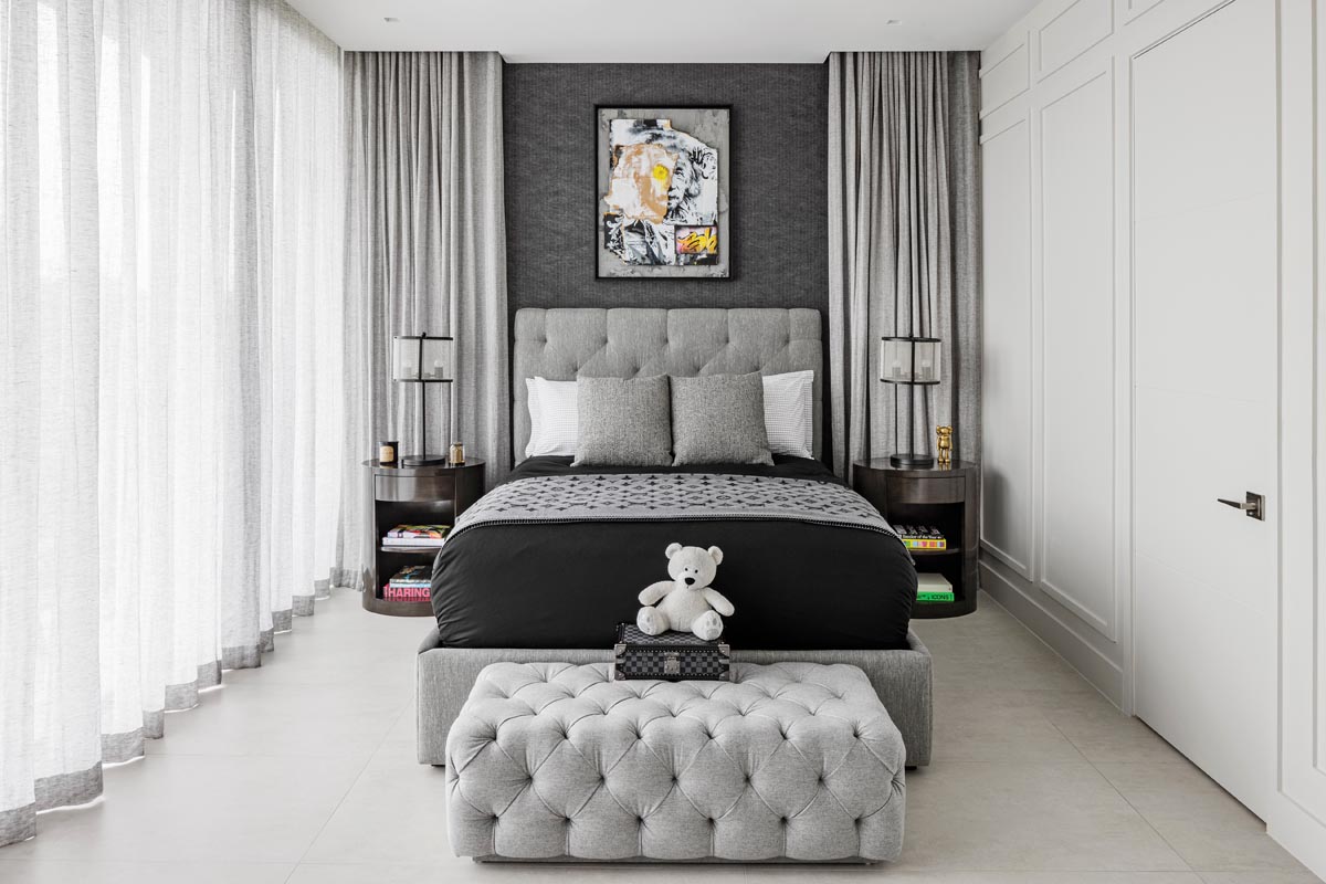 The son’s bedroom is outfitted in soft gray hues that he can grow into. The sophisticated palette is tempered with whimsical accents, including a tufted ottoman at the foot of the bed and a compelling collage over the tufted headboard.