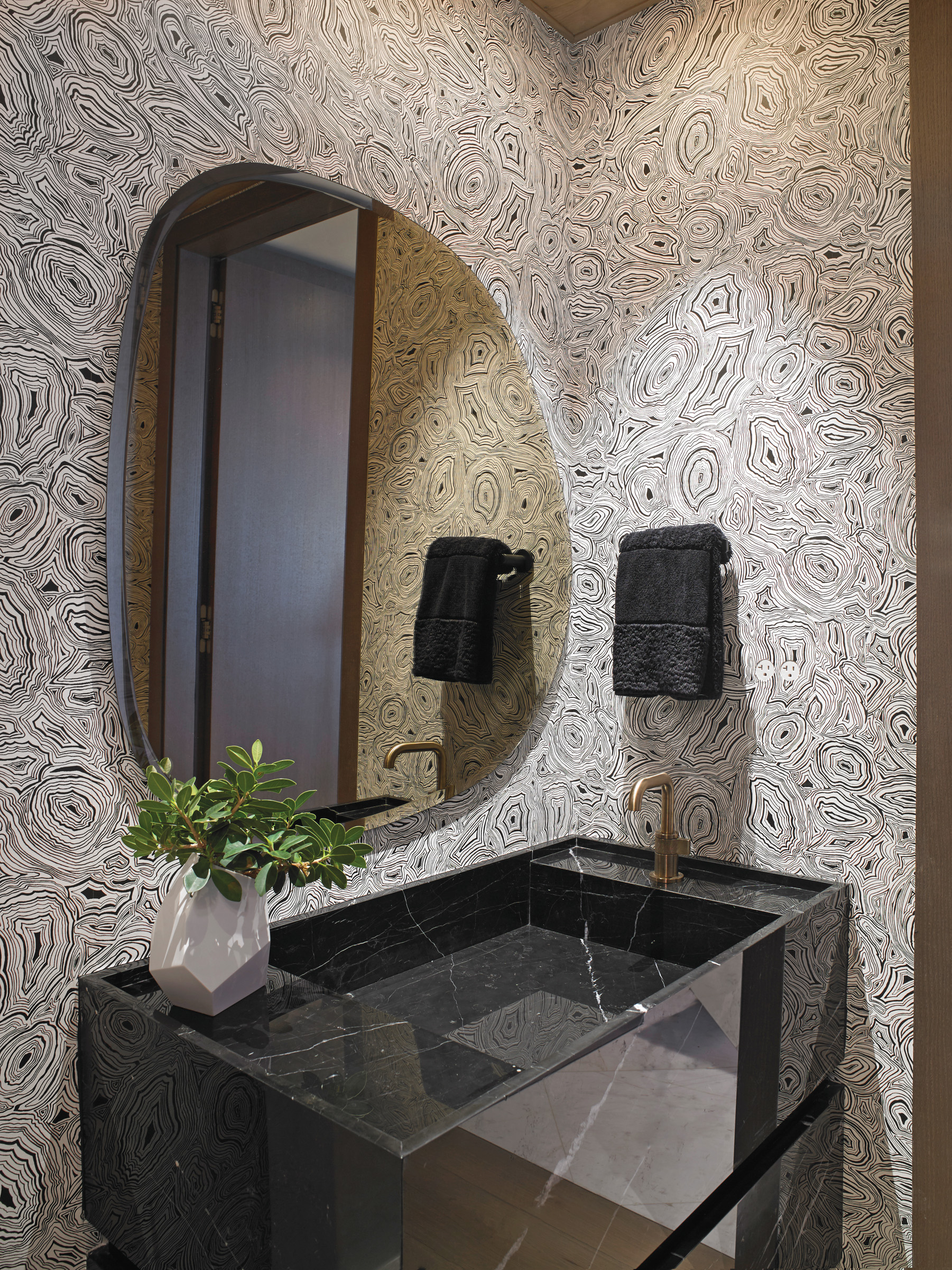 The powder room is covered in malachite-inspired wallcoverings and features a wall-mounted vanity carved from Nero Marquina marble.