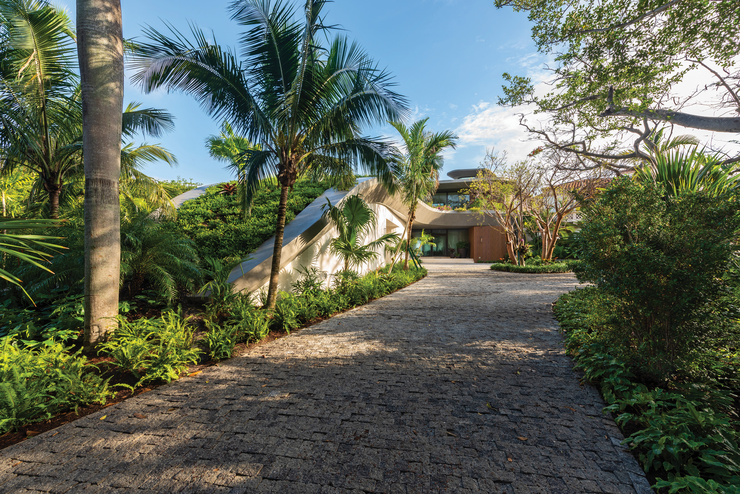 “The driveway leading to the home is composed of granite cobblestone,” says Cawley. “The stone’s split sides have a characteristic rough edge and surface, which creates a distinctive appearance.” The road is flanked by coconut palms, gumbo-limbo trees, and large-leaf philodendrons.