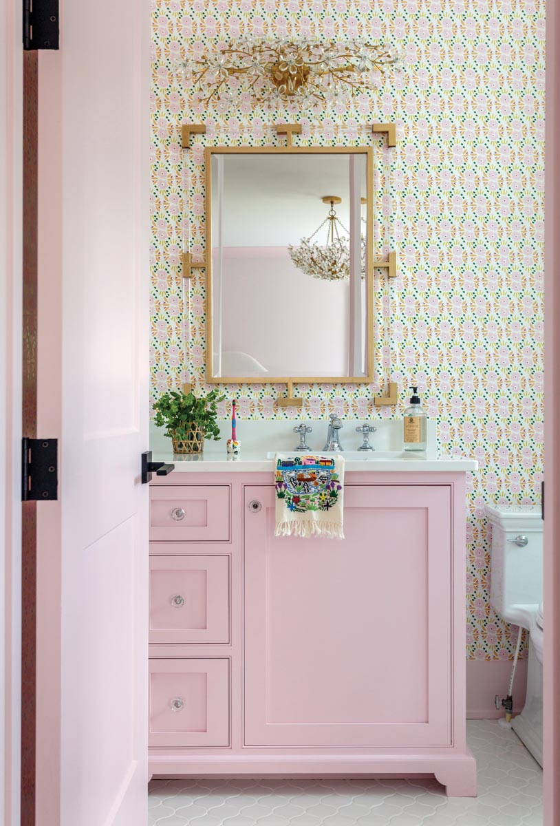 The oldest daughter’s bathroom is girlish and contemporary with a brass and acrylic mirror, and a gem-like wall sconce. The wallpaper inspired the color palette, which Leonard carried into the attached bedroom.